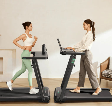 Two women use treadmills: one exercises in sportswear, while the other works on a laptop in casual attire.