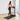 A woman in a pink sports bra and black leggings walks on a treadmill
